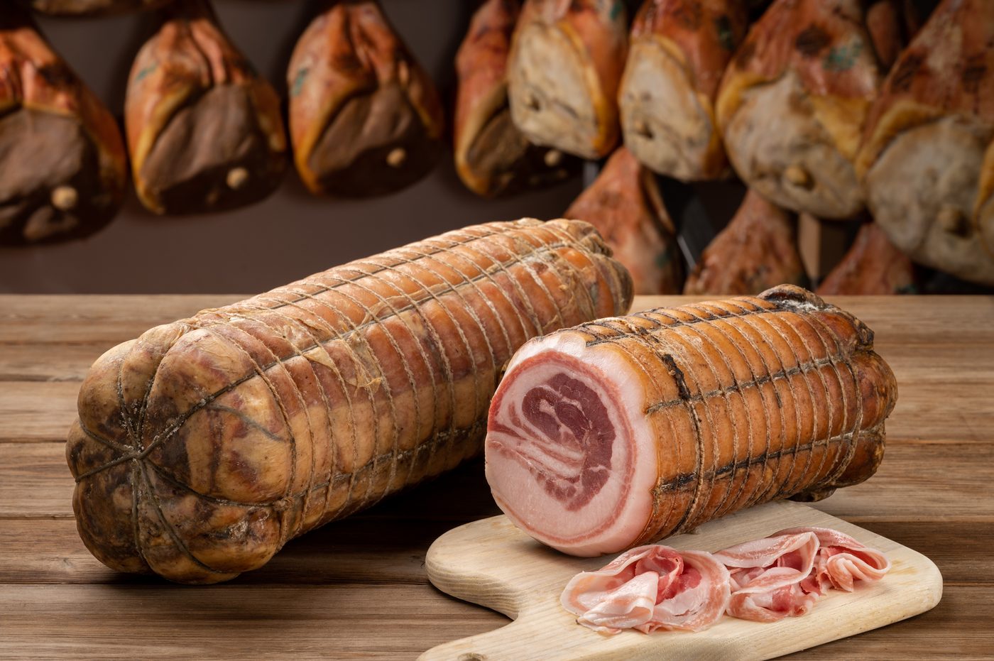 Coppa e pancetta arrotolata su tagliere con prosciutti sullo sfondo